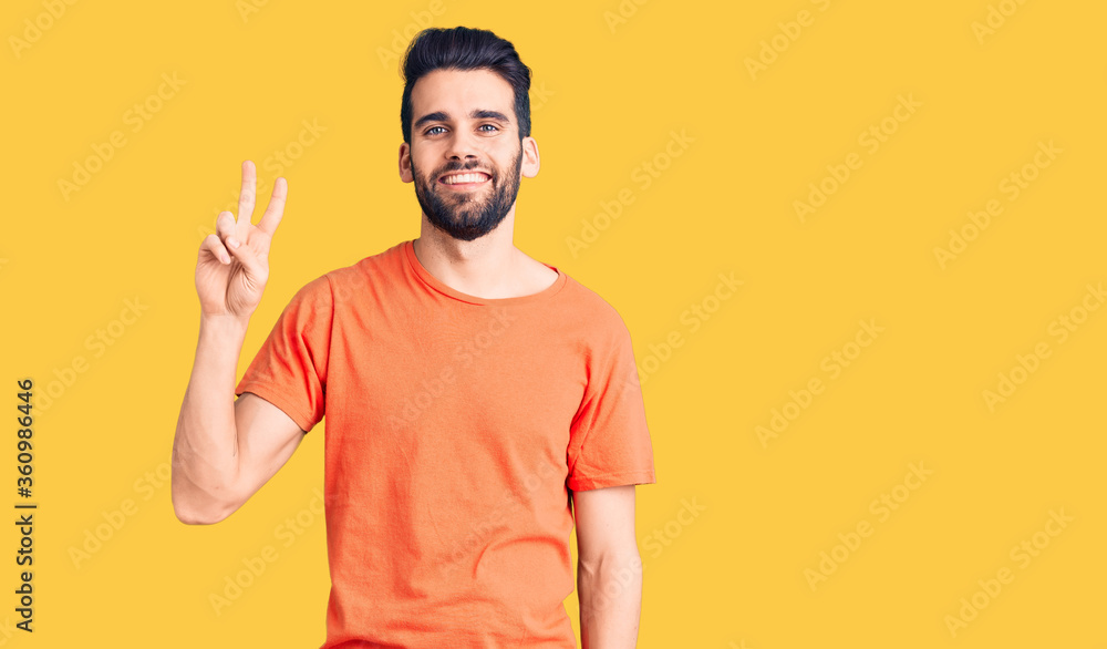 Young handsome man with beard wearing casual t-shirt smiling looking to the camera showing fingers doing victory sign. number two. Young handsome man with beard wearing casual t-shirt smiling looking to the camera showing fingers doing victory sign. number two.