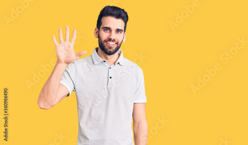 Young handsome man with beard wearing casual polo showing and pointing up with fingers number five while smiling confident and happy.