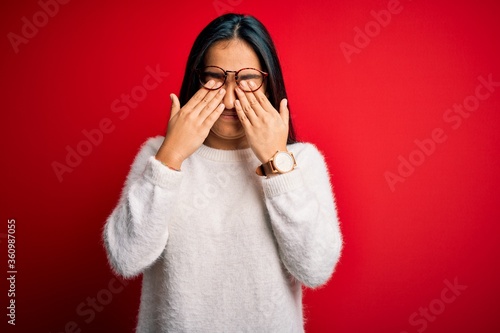 Young beautiful asian woman wearing casual sweater and glasses over red background rubbing eyes for fatigue and headache, sleepy and tired expression. Vision problem