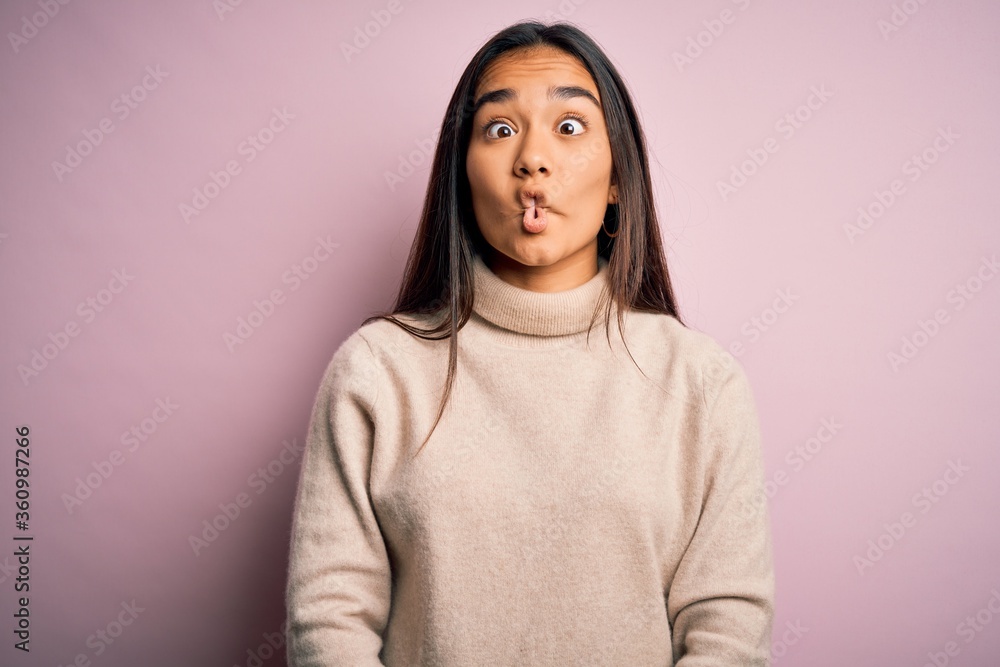 Young beautiful asian woman wearing casual turtleneck sweater over pink background making fish face with lips, crazy and comical gesture. Funny expression. Young beautiful asian woman wearing casual turtleneck sweater over pink background making fish face with lips, crazy and comical gesture. Funny expression.