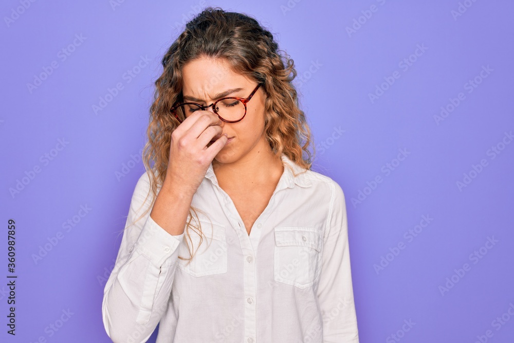 Young beautiful woman with blue eyes wearing casual shirt and glasses over purple background tired rubbing nose and eyes feeling fatigue and headache. Stress and frustration concept. Young beautiful woman with blue eyes wearing casual shirt and glasses over purple background tired rubbing nose and eyes feeling fatigue and headache. Stress and frustration concept.