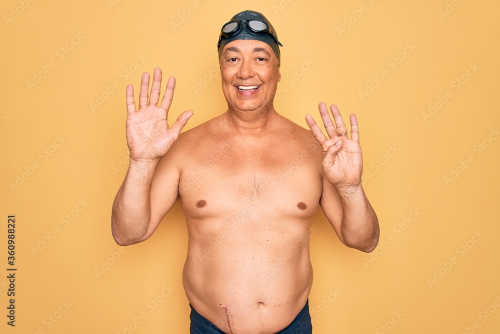 Middle age senior grey-haired swimmer man wearing swimsuit, cap and goggles showing and pointing up with fingers number nine while smiling confident and happy.