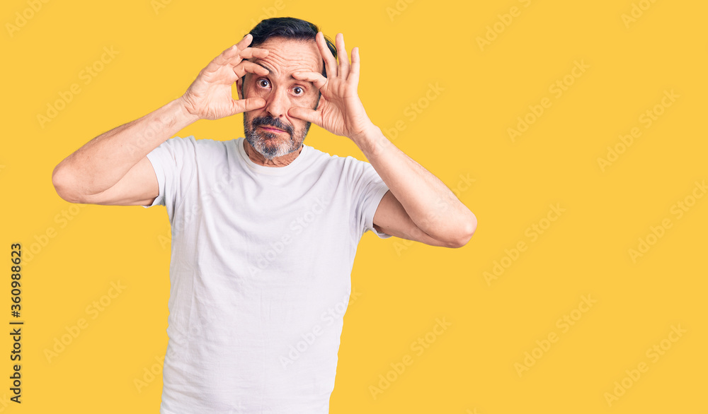 Middle age handsome man wearing casual t-shirt trying to open eyes with fingers, sleepy and tired for morning fatigue Middle age handsome man wearing casual t-shirt trying to open eyes with fingers, sleepy and tired for morning fatigue
