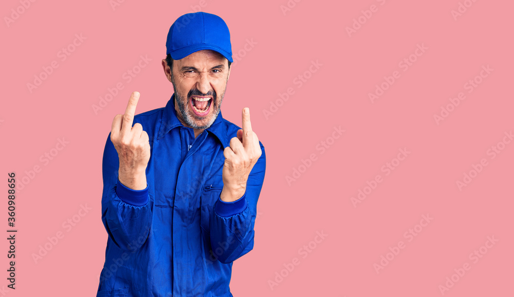 Naklejka premium Middle age handsome man wearing mechanic uniform showing middle finger doing fuck you bad expression, provocation and rude attitude. screaming excited