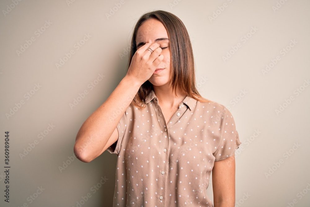 Young beautiful woman wearing casual shirt standing over isolated white background tired rubbing nose and eyes feeling fatigue and headache. Stress and frustration concept. Young beautiful woman wearing casual shirt standing over isolated white background tired rubbing nose and eyes feeling fatigue and headache. Stress and frustration concept.