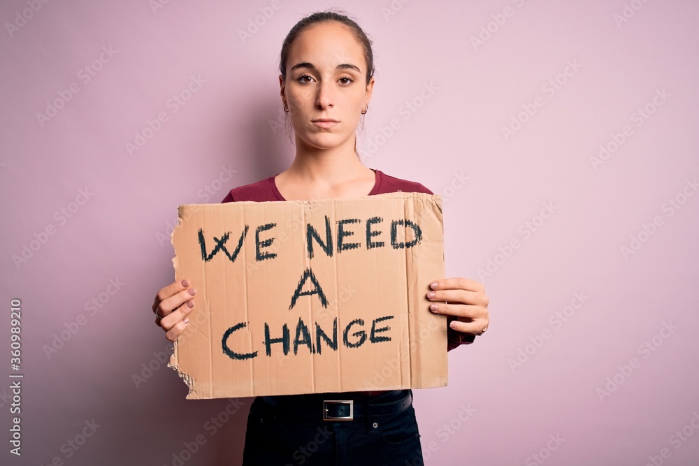 Young beautiful activist woman asking for change protesting holding banner with message with a confident expression on smart face thinking serious Young beautiful activist woman asking for change protesting holding banner with message with a confident expression on smart face thinking serious