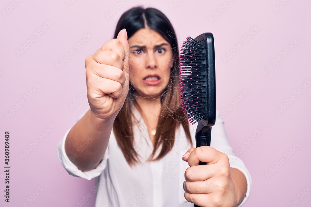 Young beautiful woman agry and worried for capillary problem. Holding hairbrush with tangled hair standing over isolated pink background Young beautiful woman agry and worried for capillary problem. Holding hairbrush with tangled hair standing over isolated pink background