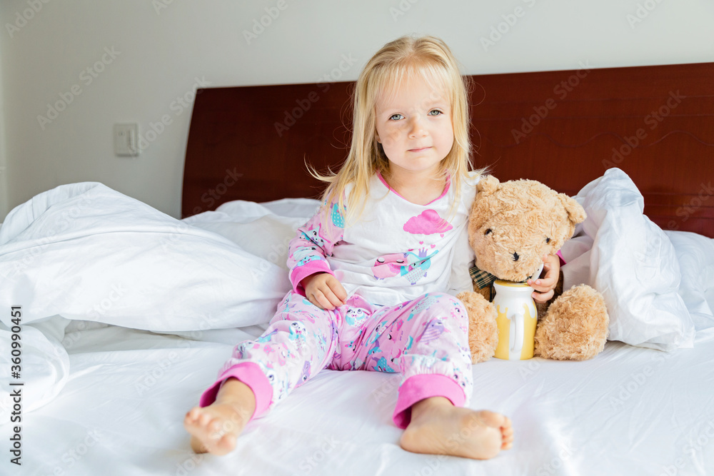 Cute little girl with blonde hair sitting on the bed with stuffed teddy bear. Happy childhood. Stay at home during coronavirus covid-19 pandemic quarantine concept. Cute little girl with blonde hair sitting on the bed with stuffed teddy bear. Happy childhood. Stay at home during coronavirus covid-19 pandemic quarantine concept.