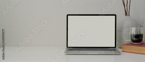 Simple home office with mock-up laptop, book, coffee cup, decorations and copy space on white desk