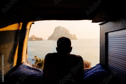 Fototapeta Man lying in a caravan and enjoying the sunset on a beach