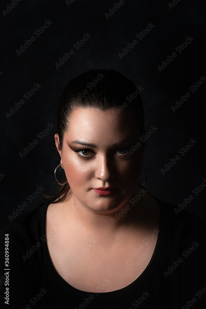 close-up of a beautiful portrait of a plus-size girl with a serious, purposeful and strong expression on a black background