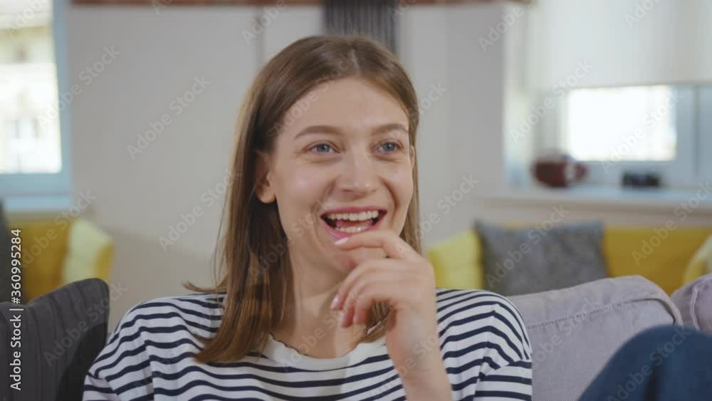 Smiling beautiful woman sitting in room on the sofa watching the funny comedy movie or tv show and laugh relaxation happy movie film entertainment stylish slow motion Smiling beautiful woman sitting in room on the sofa watching the funny comedy movie or tv show and laugh relaxation happy movie film entertainment stylish slow motion
