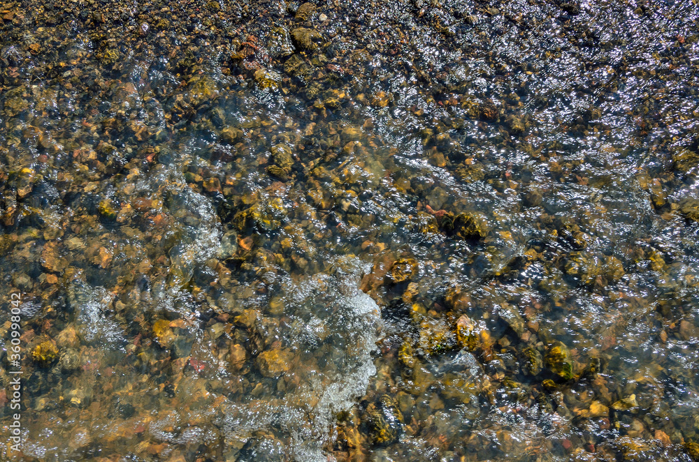 Cool freshness of mountain river fast stream in sunny summer day. Colorful pebbles under transparent clear water, sun glare on the surface of water Cool freshness of mountain river fast stream in sunny summer day. Colorful pebbles under transparent clear water, sun glare on the surface of water