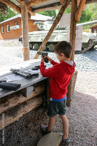 young boy aiming from pistol to the paper target in the outdoor shooting gallery