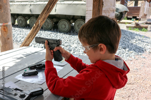 Fotografía young boy aiming from pistol to the paper target in the outdoor shooting gallery