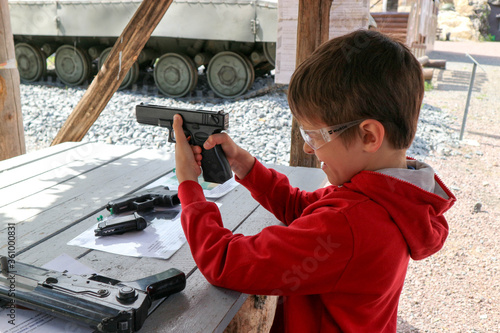 young boy aiming from pistol to the paper target in the outdoor shooting gallery