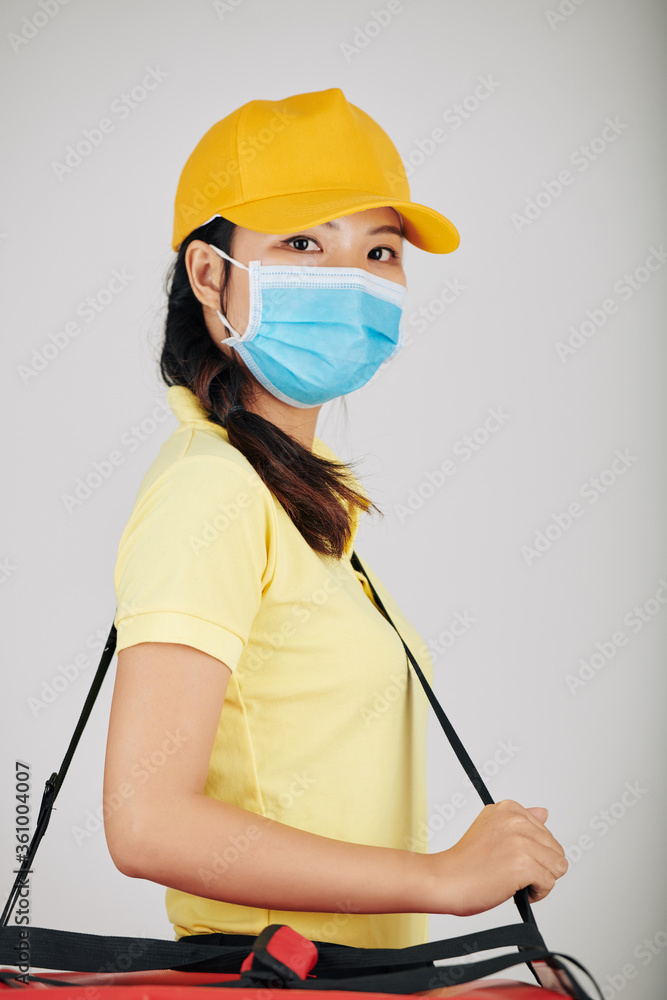 Portrait of contactless delivery service worker in medical mask carrying portable refrigerator and looking at camera Portrait of contactless delivery service worker in medical mask carrying portable refrigerator and looking at camera