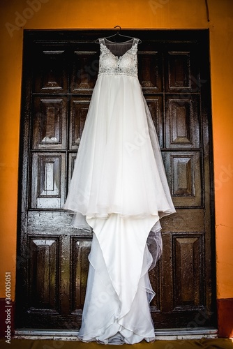 Vertical shot of a long white  wedding dress on a hanger hanged against a wooden door photo