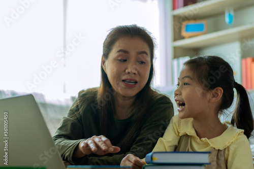 A Beautiful Asian mother busy working while looking after and teaching her children on a laptop computer at home