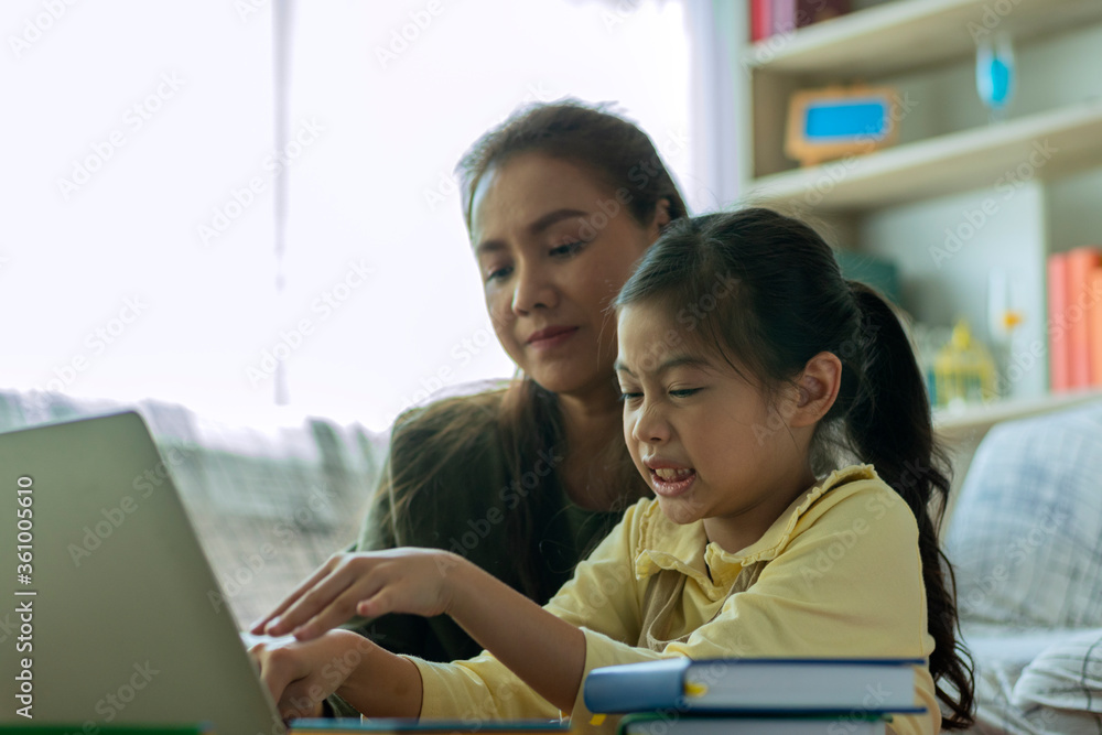 Fototapeta premium A Beautiful Asian mother busy working while looking after and teaching her children on a laptop computer at home