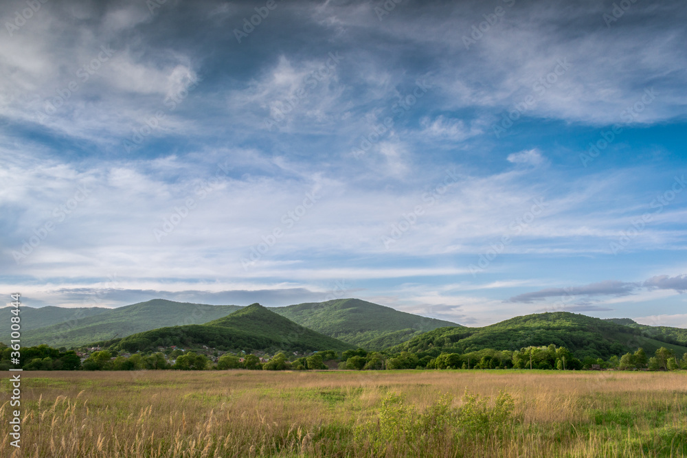 Not high mountains covered with green forest and green meadow against a blue sky with clouds Not high mountains covered with green forest and green meadow against a blue sky with clouds