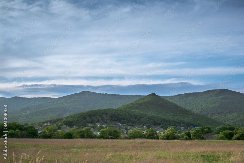 Not high mountains covered with green forest and green meadow against a blue sky with clouds