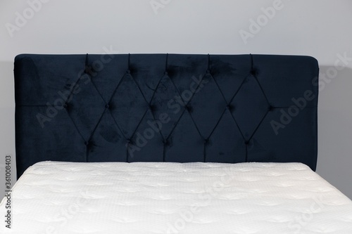 Closeup shot of a bed with dark blue fabric headboard and white mattress