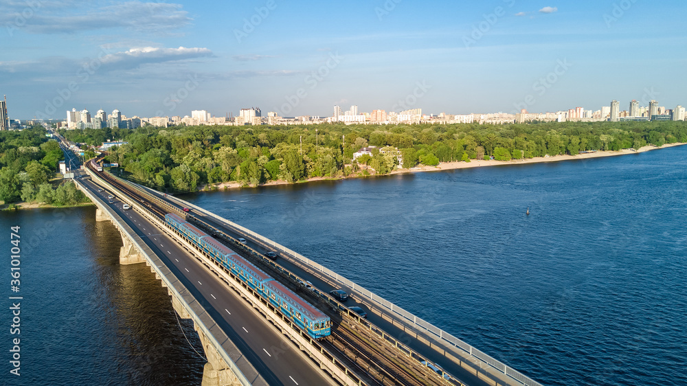 Aerial drone view of Metro railway bridge with train and Dnieper river from above, skyline of city of Kyiv, Kiev cityscape, Ukraine
