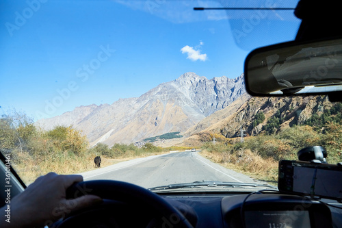 Tbilisi, Georgia - October 25, 2019: Car vindow, hand of woman on steering wheel and view to the road and autumn mountain landscape © keleny
