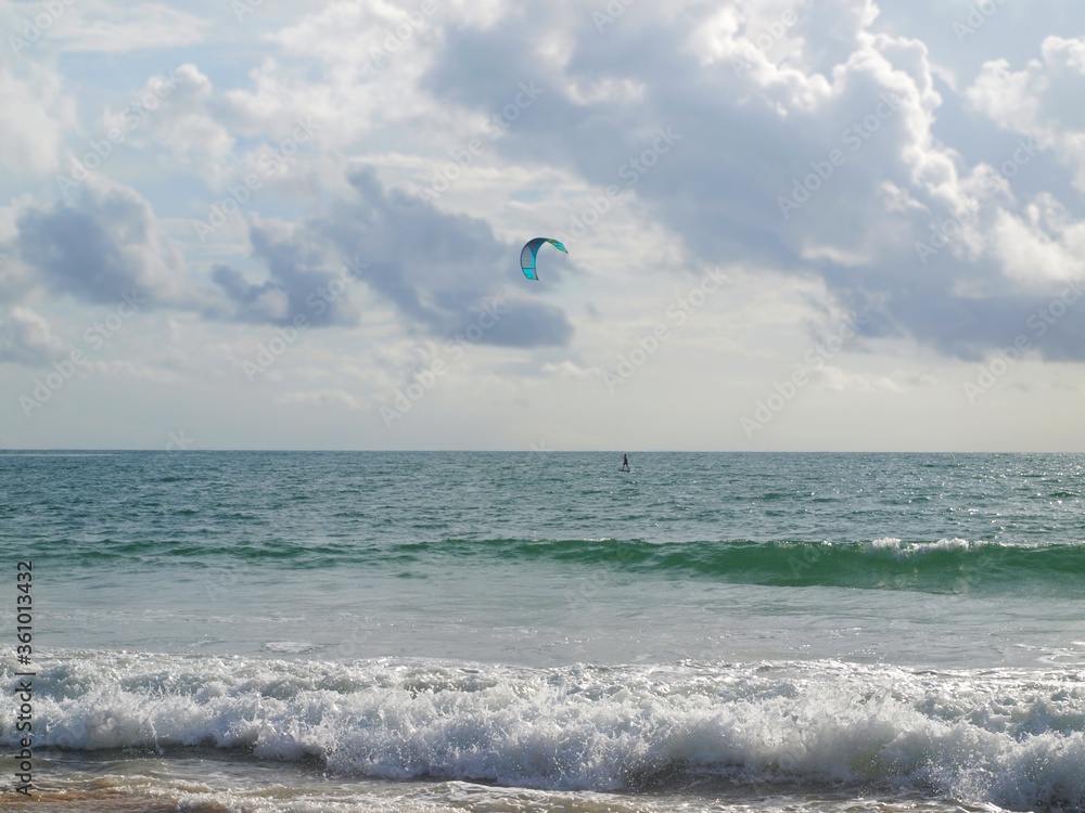 Beautiful seascape and water sport activity. Kitesurfing, kite surfing on the sea. Amazing sky with clouds and bright blue parasite. Ocean, coast, sand, turquoise waves. Kite boarding, kiteboarding