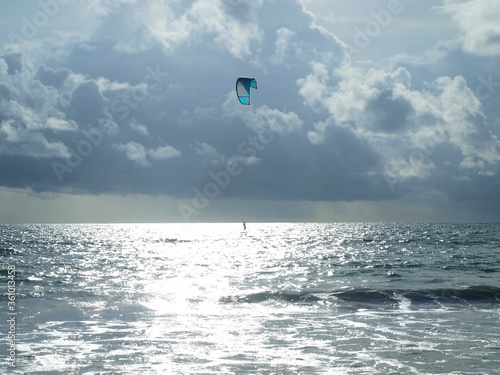 Scene of kite surfing on the atlantic ocean in the ray of the sun. Lonely kitesurfer on the beautiful cloudy sky background. Seascape, extreme water sport, storm weather. Kitesurfing, Kiteboarding.