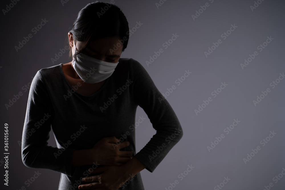 Asian woman wearing protective face mask was sick with stomach ache holding hands pressing her abdomen isolated on background.