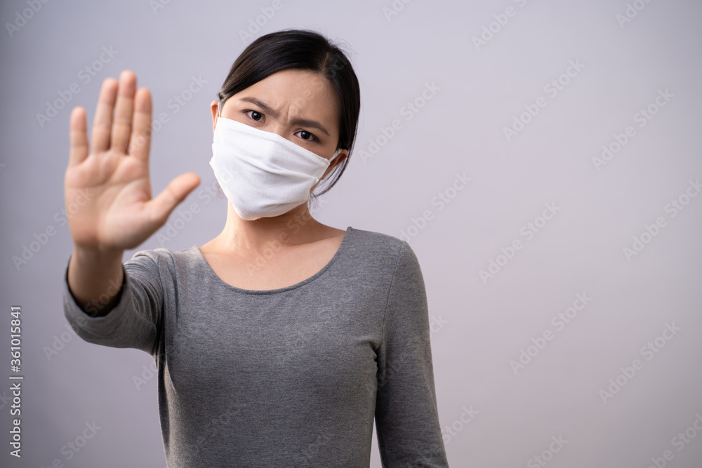 Asian woman wearing protective face mask showing hand making stop sign standing isolated on background. Asian woman wearing protective face mask showing hand making stop sign standing isolated on background.