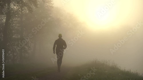 Athlete running on a gravel road during a foggy, spring sunrise in the countryside. photo