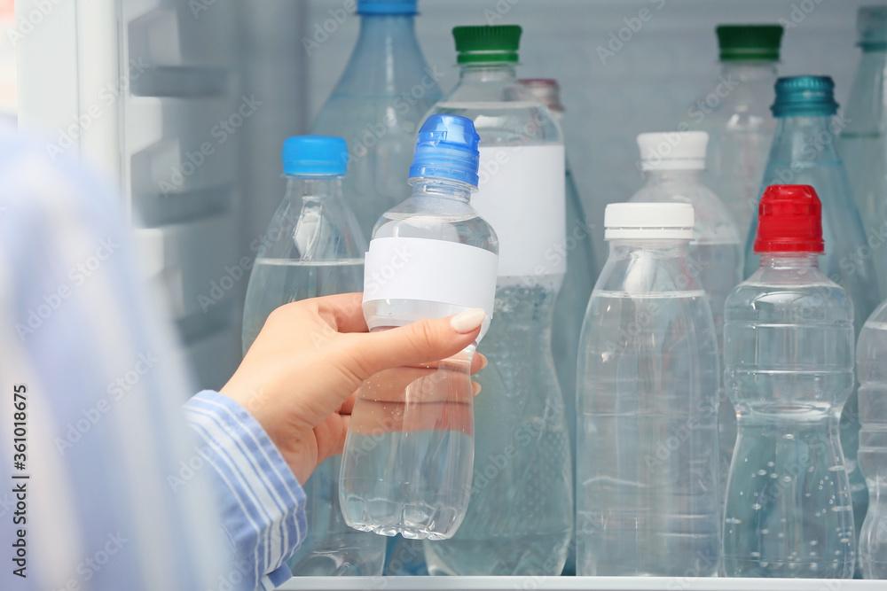 Woman taking bottle of water from fridge in shop Woman taking bottle of water from fridge in shop
