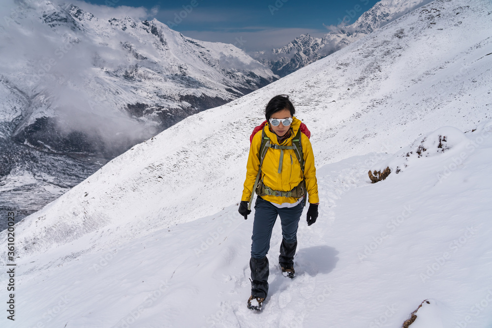 Young Asian woman trekking in Langtang valley after heavy snow storm. A woman trekking on trail that covered by fresh snow. Himalaya mountains range, Nepal