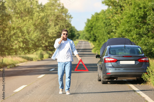 Young man with emergency stop sign near broken car on road © Pixel-Shot