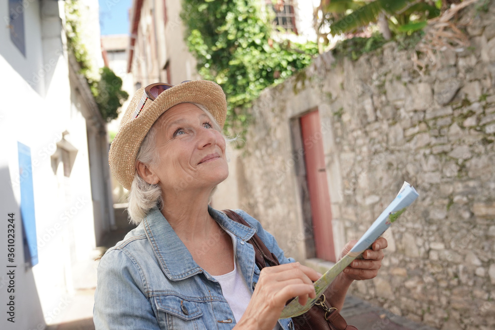 Portrait of senior woman with hat visiting touristic town, reading city map