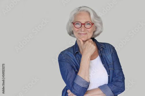 Portrait of senior woman wearing blue jeans shirt and red eyeglasses, isolated