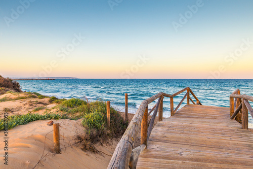 wooden access over the dunes to the beach with a view of the horizon over the sea at sunset. Guardamar, Alicante. Spain © kemirada