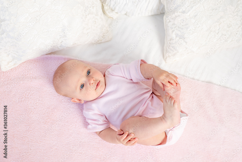 a small baby girl 6 months old is lying on a white and pink bed at home, looking away, top view, place for text a small baby girl 6 months old is lying on a white and pink bed at home, looking away, top view, place for text