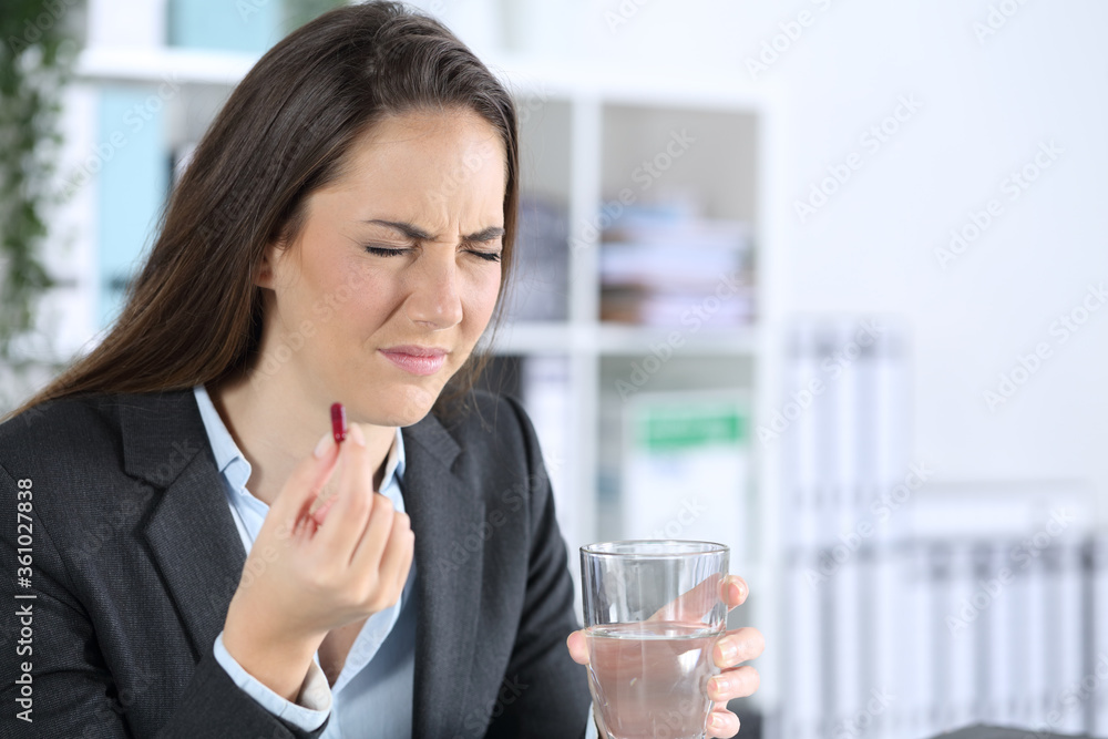 Executive holding painkiller pill and water glass at office