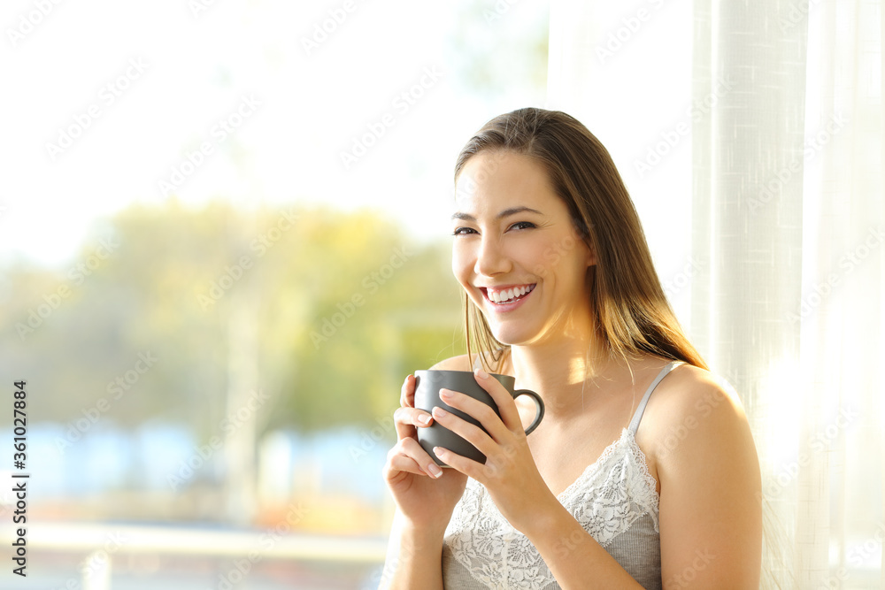 Happy woman at home holding a coffee cup looks at you Happy woman at home holding a coffee cup looks at you