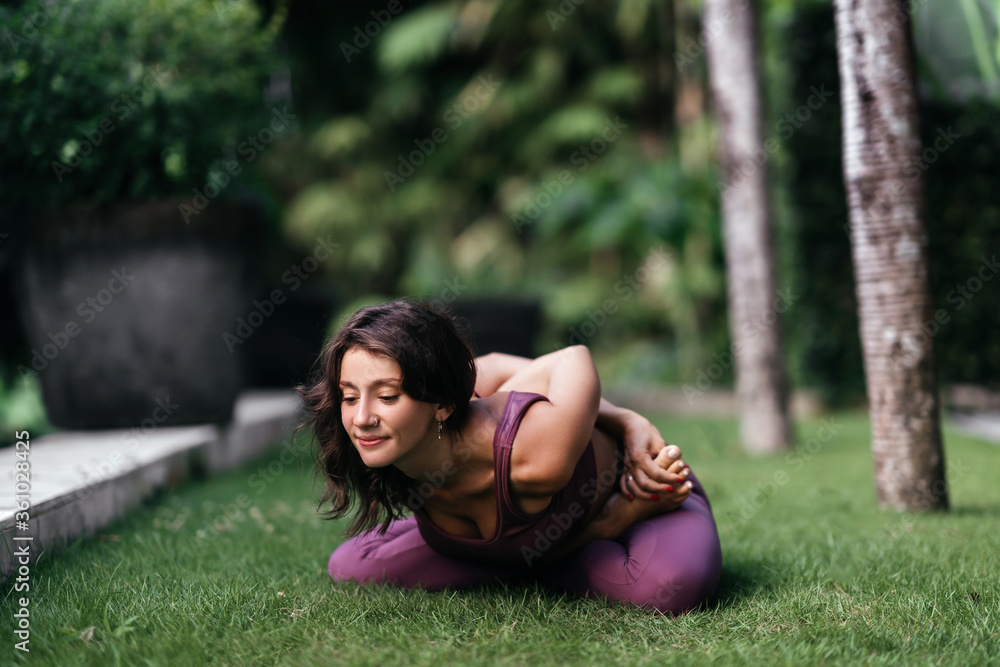 Woman practicing yoga performing yoga-asanas outdoors. Young attractive slim fitness girl in bodysuit relaxing and doing exercises. Woman practicing yoga performing yoga-asanas outdoors. Young attractive slim fitness girl in bodysuit relaxing and doing exercises.