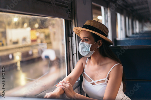 Young brunette woman traveling in Thailand on train during pandemic Coronavirus. 20s Hispanic in a protective mask wear summer sleeveless clothes and backpack in Asia.