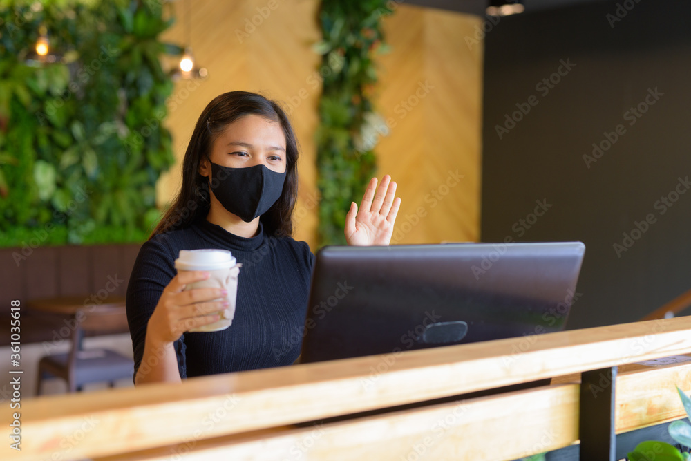 Φωτογραφία Young Asian businesswoman with mask video calling and sitting with distance insi