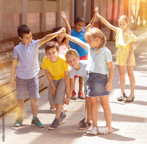Group of positive schoolchildren holding hands up and playing