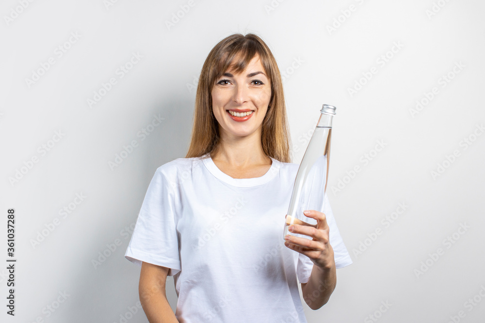 Young woman holds a bottle with clear water on a light background. Banner. The concept of thirst, heat, health and beauty care, water balance Young woman holds a bottle with clear water on a light background. Banner. The concept of thirst, heat, health and beauty care, water balance