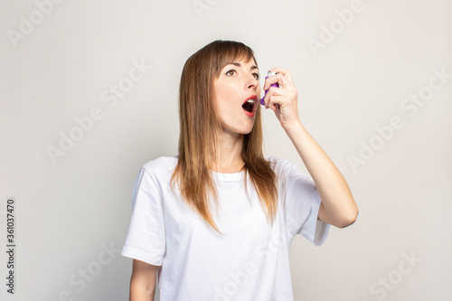 young woman with an open mouth in her hand holds an inhaler and atomizes on a light background. Banner. Concept for easier breathing, treatment of asthma, pharynx, larynx, trachea