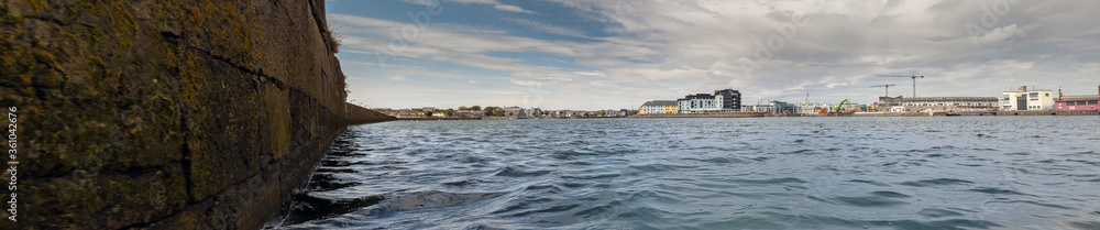 View on Galway city from river Corrib, low angle, panorama image. The long walk and dock area, Warm sunny day, Cloudy sky over city